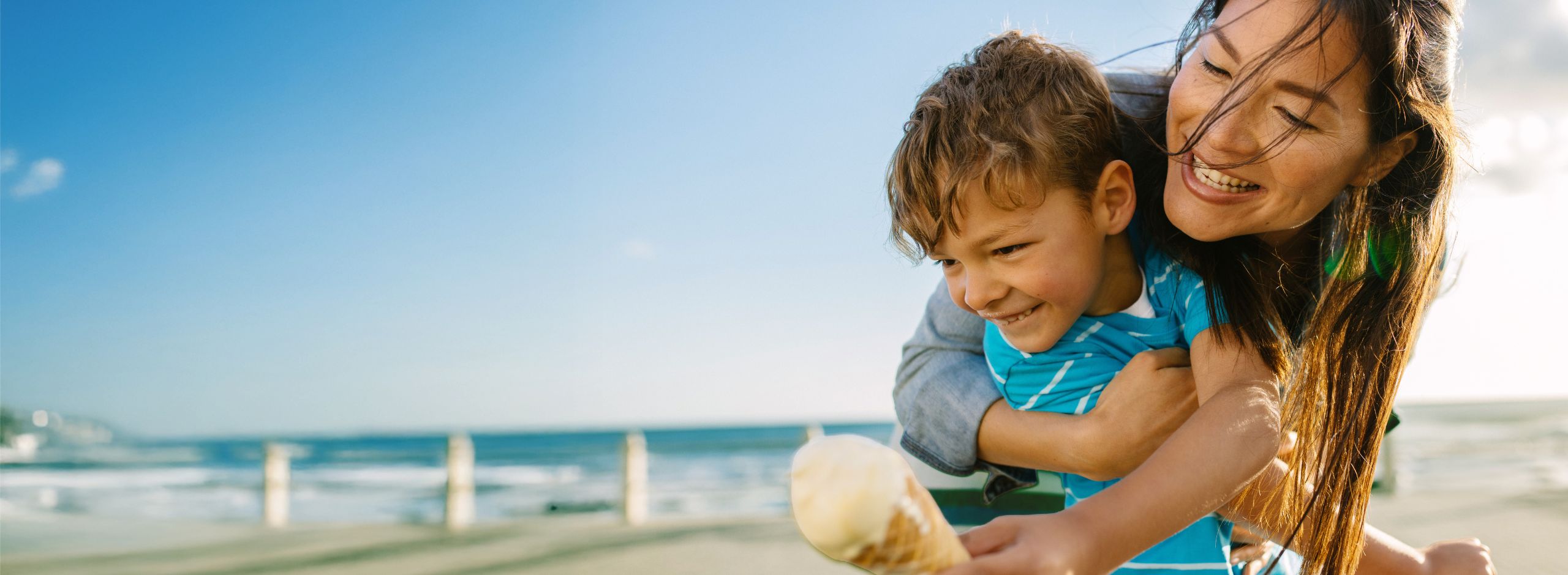 A woman hugging a young boy with an ice cream on the beach.
